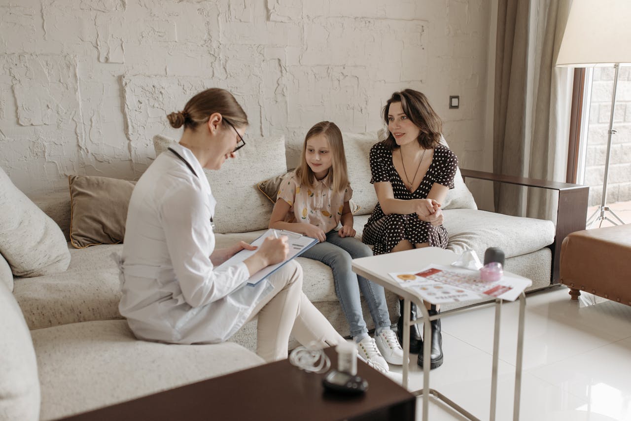 services-03 A doctor consults with a mother and daughter in a cozy indoor setting.